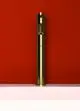 Hohes, glänzendes Standventil in Brushed Gold-Finish vor roter Wand. Der Ärmelauslass ist sichtbar. Ideal Standard ist als Marke erkennbar.
